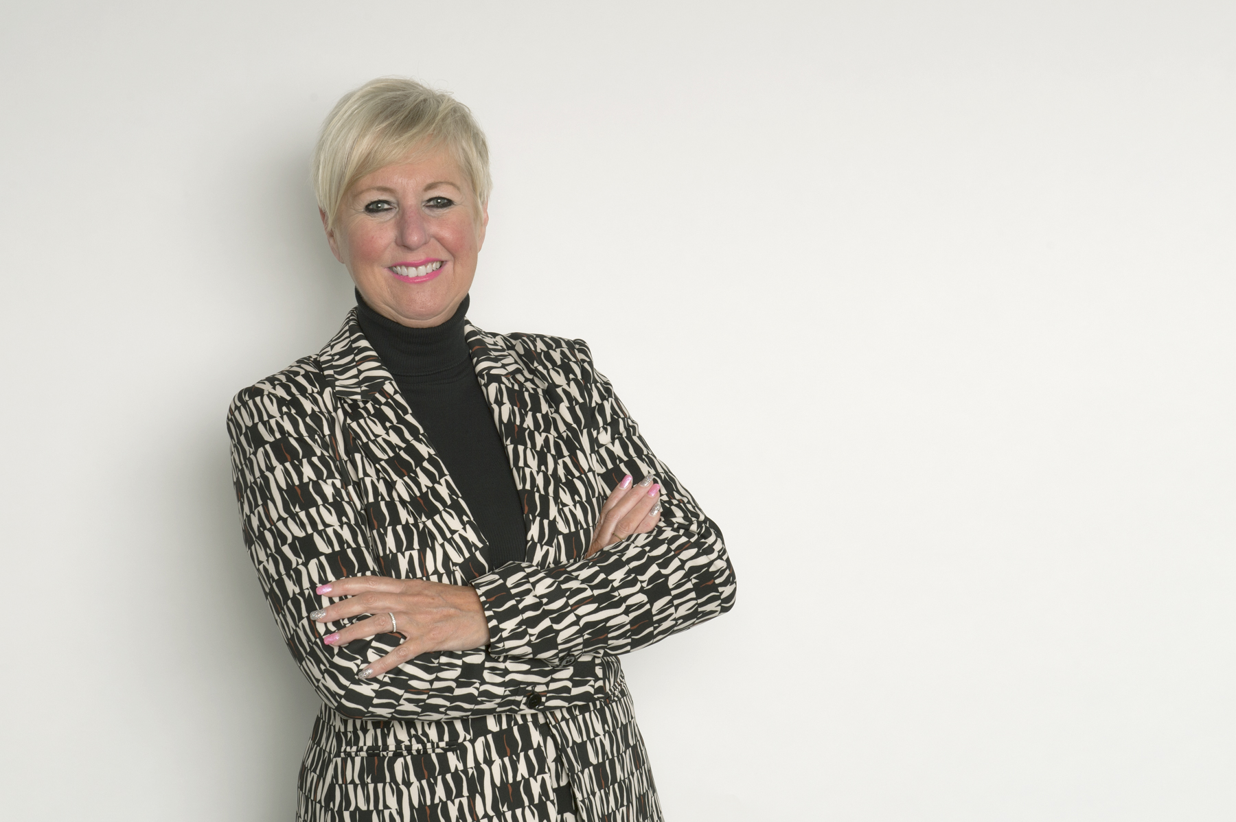 CEO Diane Wake smiles at the camera, arms crossed leaning against a blank white wall