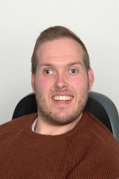 Headshot of Alex Giles smiling at the camera.. Alex is wearing a burgundy jumper