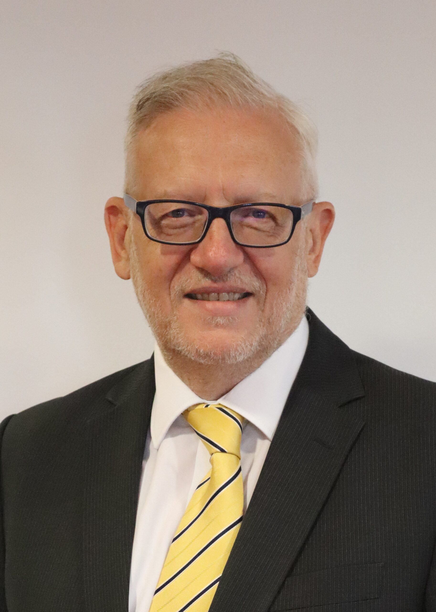 Headshot of Peter Featherstone smiling, wearing a black suit jackets and yellow tie