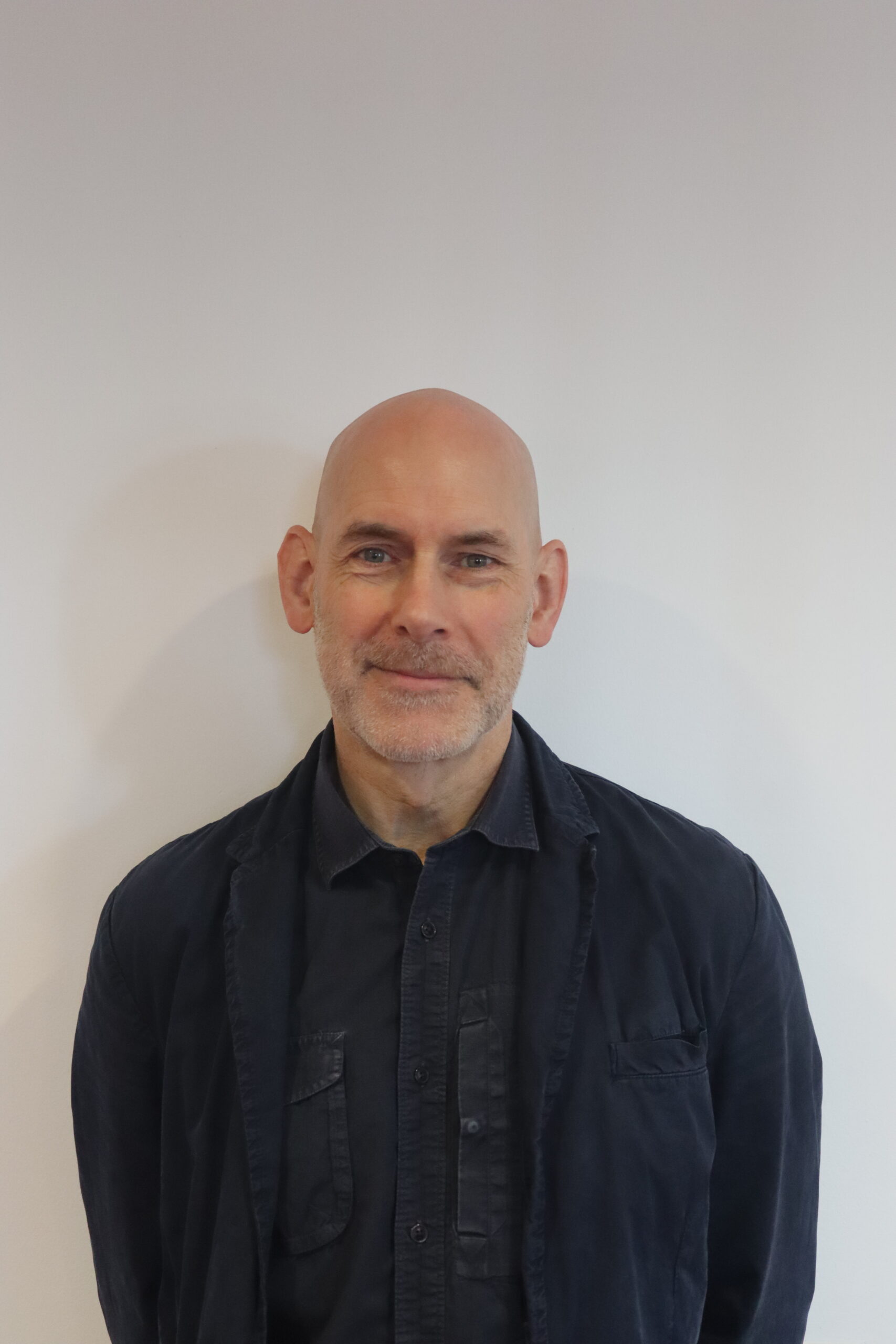 Headshot of Mick Laverty, he is facing the camera and smiling, he wears a navy blue shirt and jacket