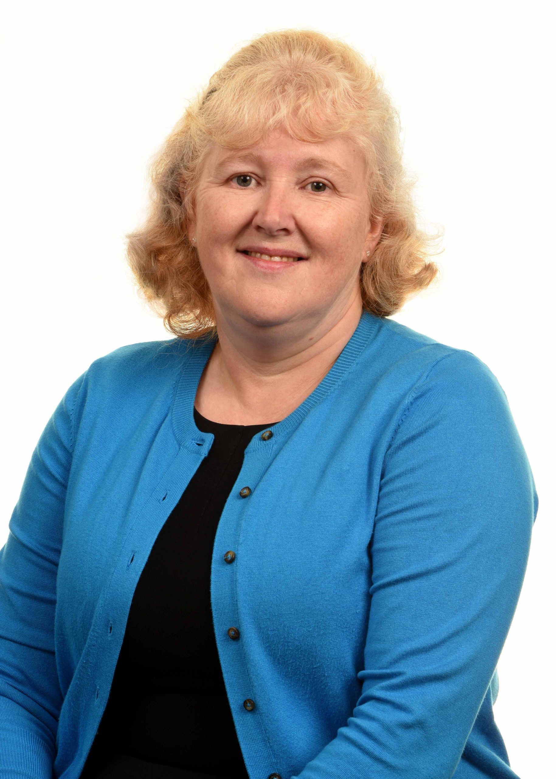 A lady with blonde hair wearing a blue cardigan and black top smiling at the camera.