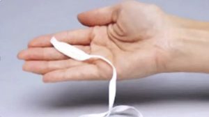 A hand holding a pessary, a small white piece of fabric containing hormones, with a string on the bottom end.